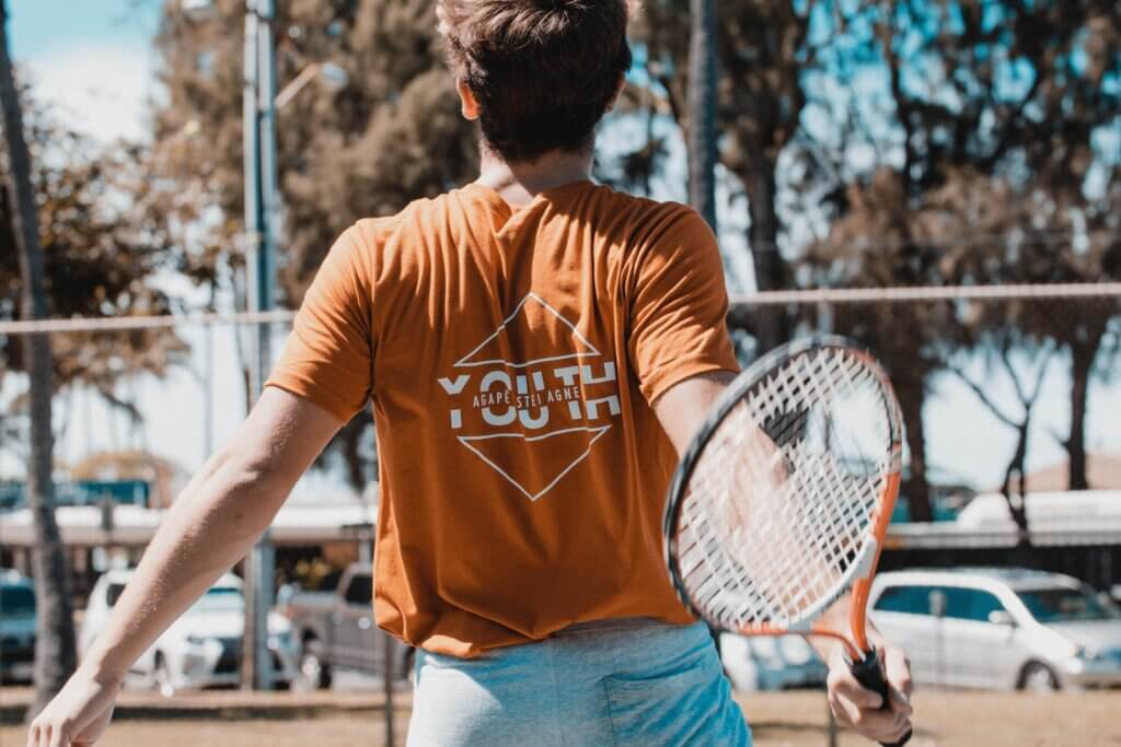 man in brown t-shirt holding a tennis racket